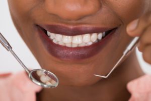 A close up image of a patient's mouth with dental tools approaching, illustrating a healthy smile during an examination.